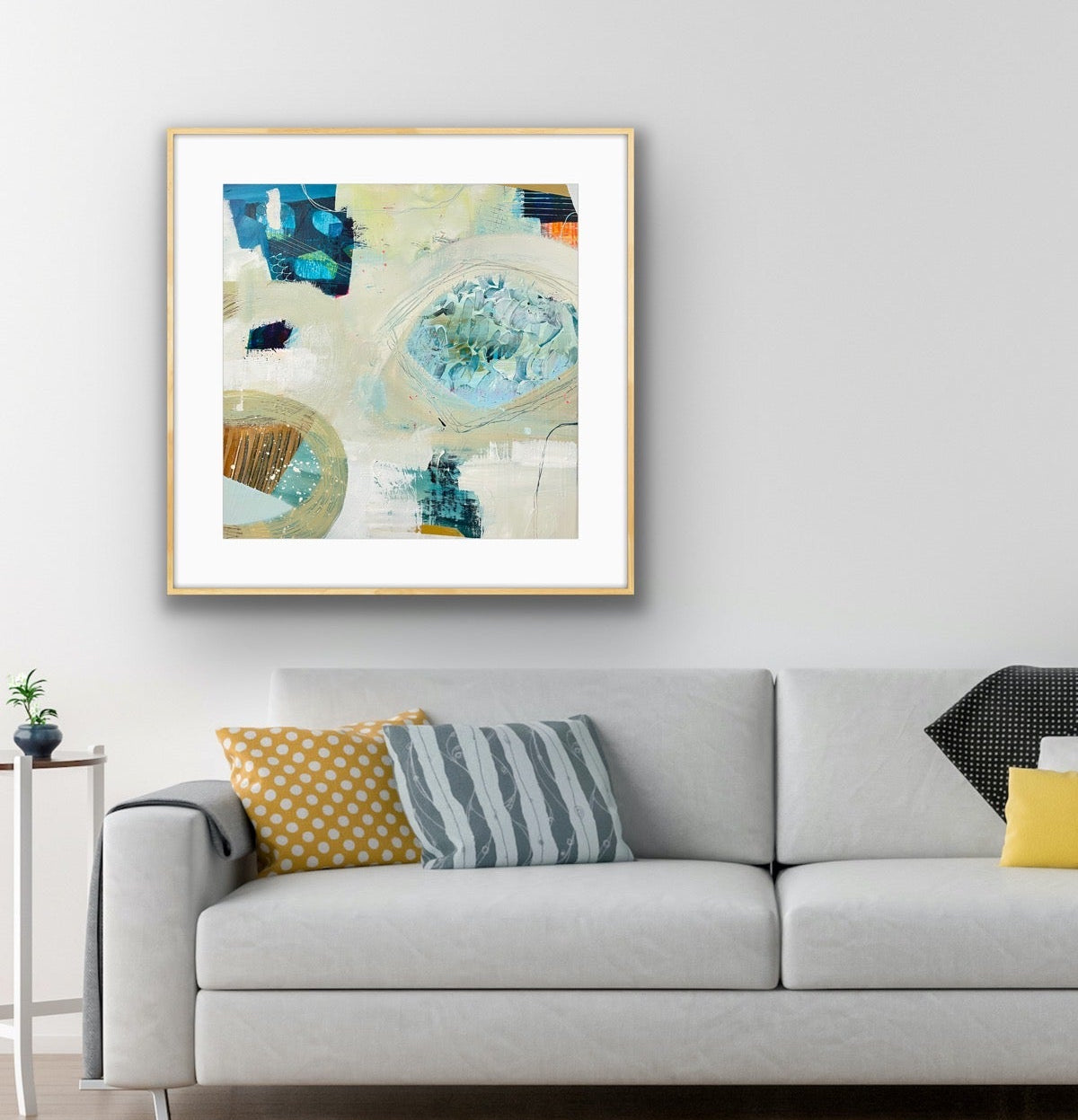 Modern living room with a gray sofa, colorful pillows, and an abstract art print "Beachcombing" on the wall.