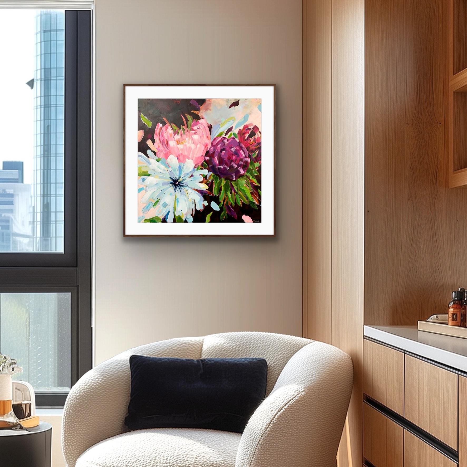 A framed floral art print from alisonGilbertart.com hangs on a beige wall in a modern living room setting, featuring a white textured armchair with a dark blue pillow and a wooden cabinet below.