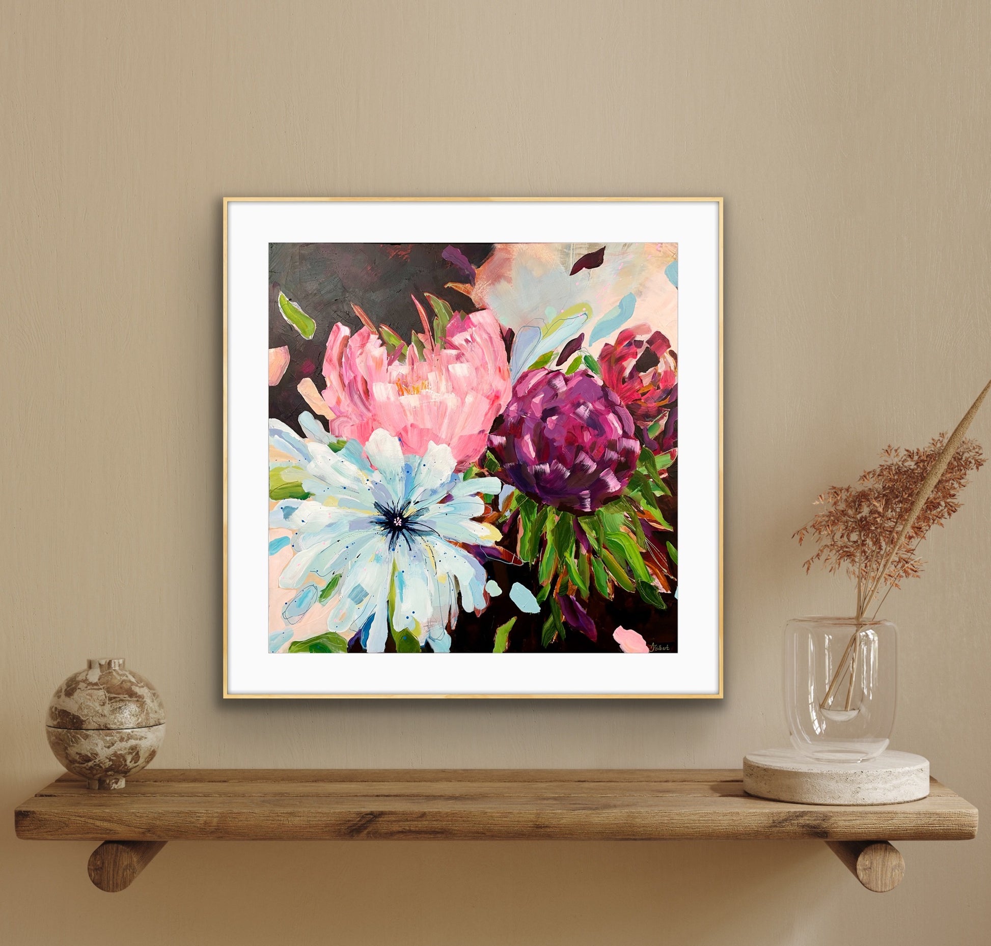 A framed floral art print from alisongilbertart.com featuring pink, purple, and light blue flowers with green leaves, displayed on a wooden shelf against a beige wall with decorative objects.