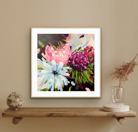 A framed floral art print from alisongilbertart.com featuring pink, purple, and light blue flowers with green leaves, displayed on a wooden shelf against a beige wall with decorative objects.