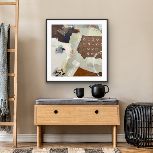 Framed neutral abstract art 'Echoes" Giclee Print by Alison Gilbert Art, above a wooden side table with a cushion and decorative items.