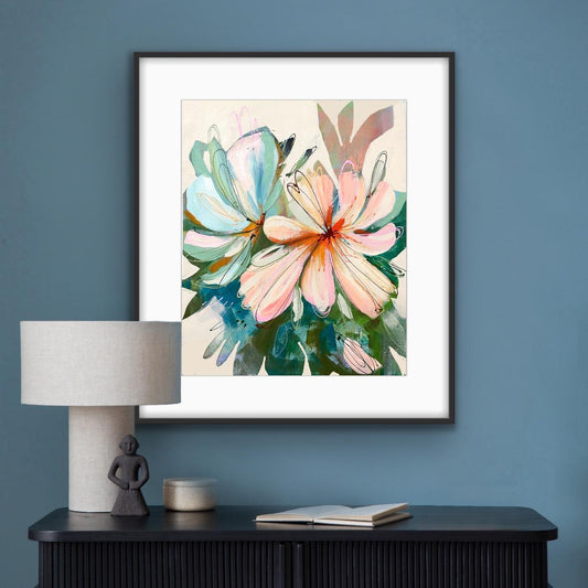 Framed floral print "Peach Perfect'on a blue wall above a black cabinet with a white lamp.