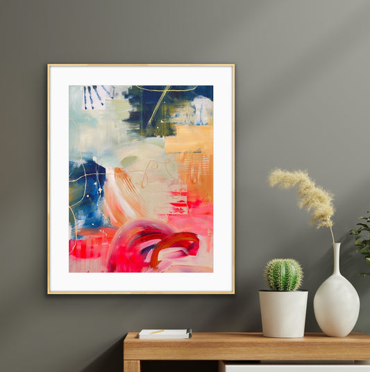 Framed abstract art print 'Red Moon Rising' on a wall with a table and decorative items below.