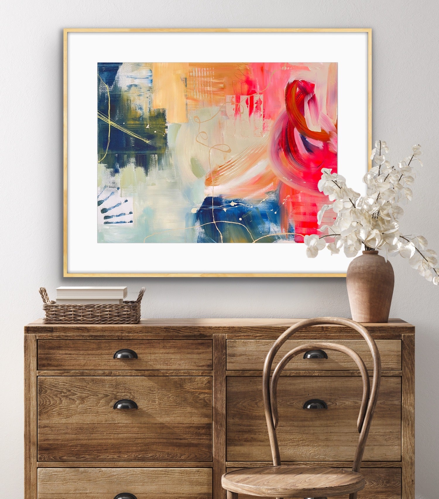 Abstract Framed Art Print on Paper 'Red Moon Rising' above a wooden dresser with a chair and vase.