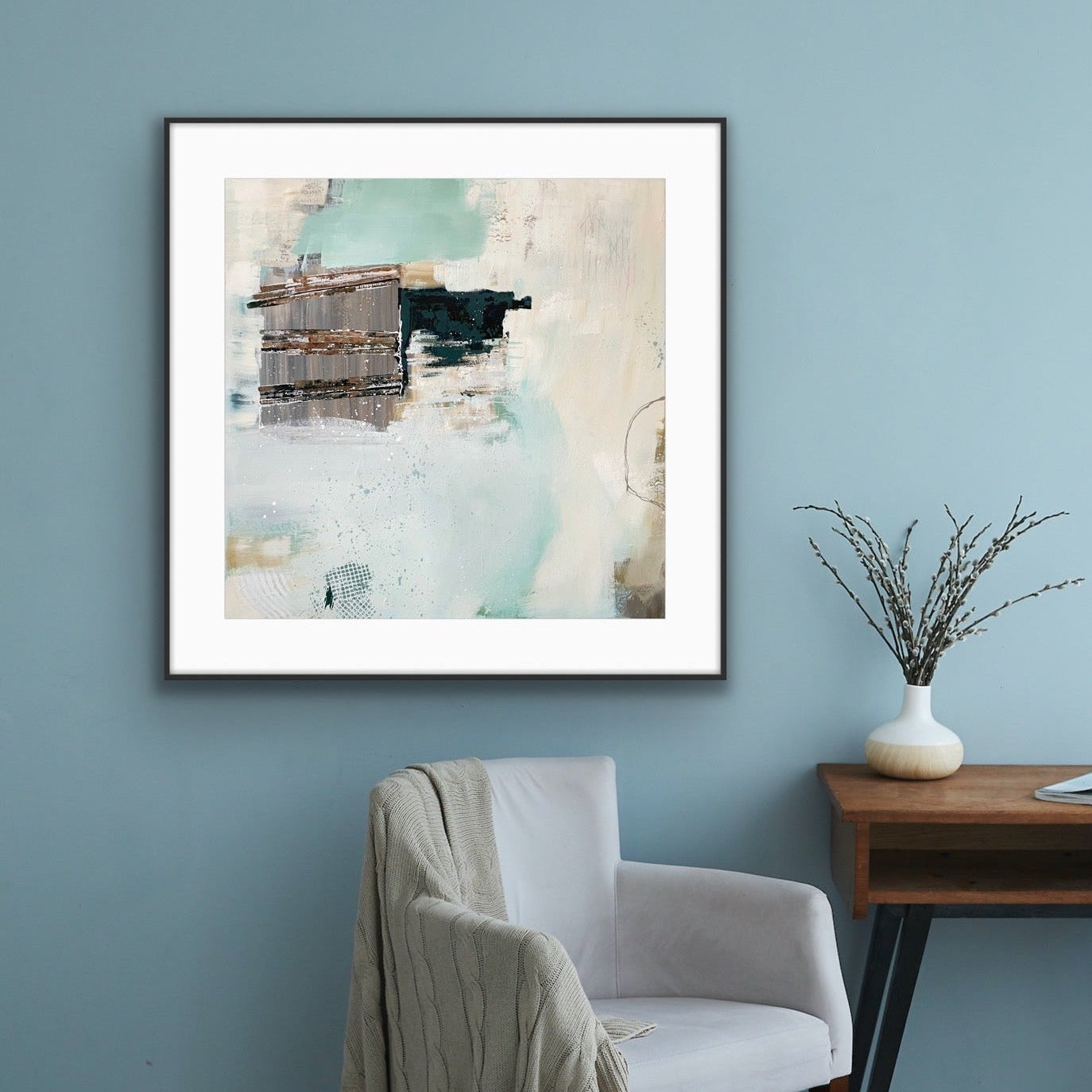 Framed abstract art print "Seafoam's Echo" by Alison Gilbert Art, on a blue wall above a chair with a blanket draped over it.