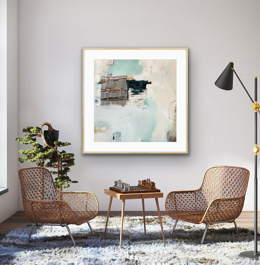 Modern living room with wicker chairs, a small table, and an abstract art print, "Seafoam's Echo," by Alison Gilbert Art, on the wall.