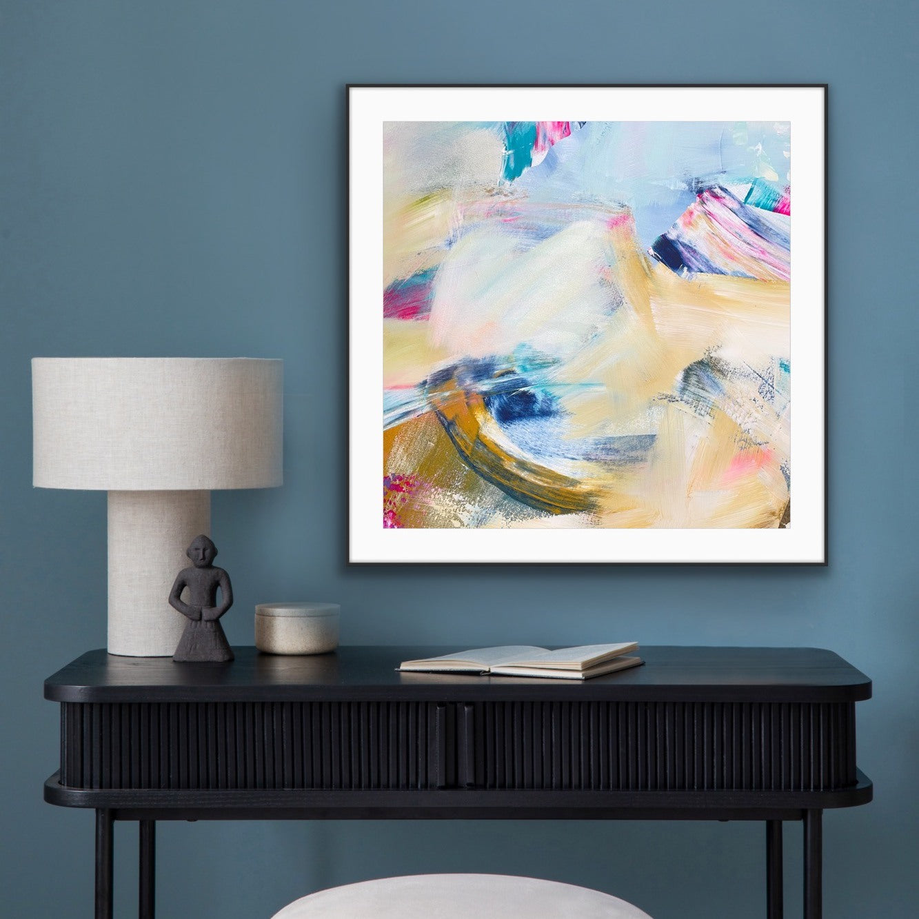 Framed abstract art print "Summer  Breeze" on a wall above a black console table with decorative items.