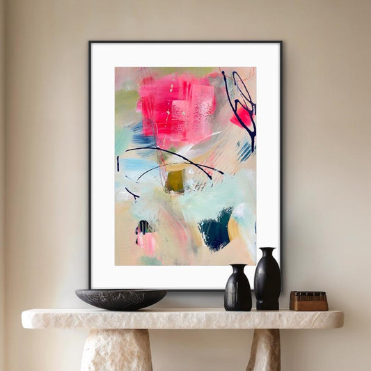 Framed abstract art print 'Unexpected arrival' on a wall above a console table with decorative items.