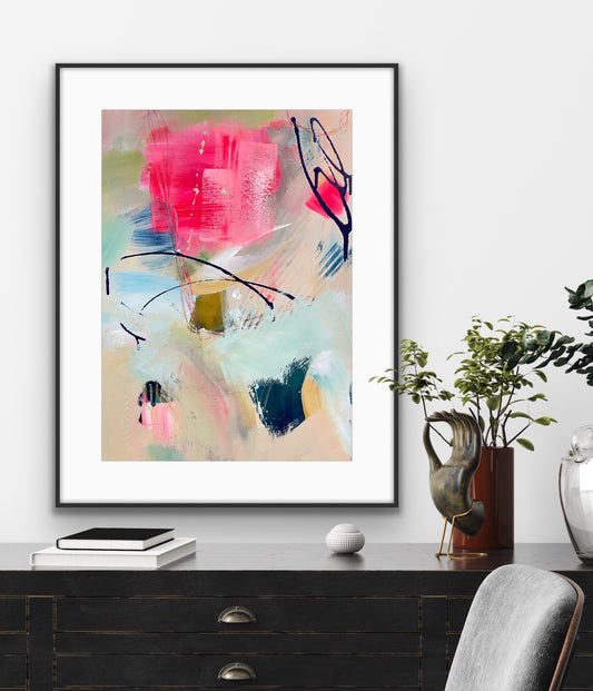 Abstract art print in a black frame on a wall above a desk with decor items.